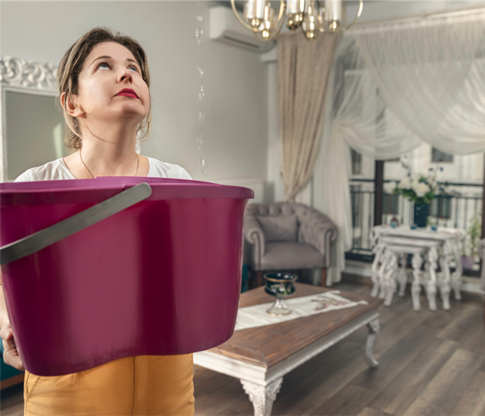 woman holding bucket to catch water dripping from ceiling