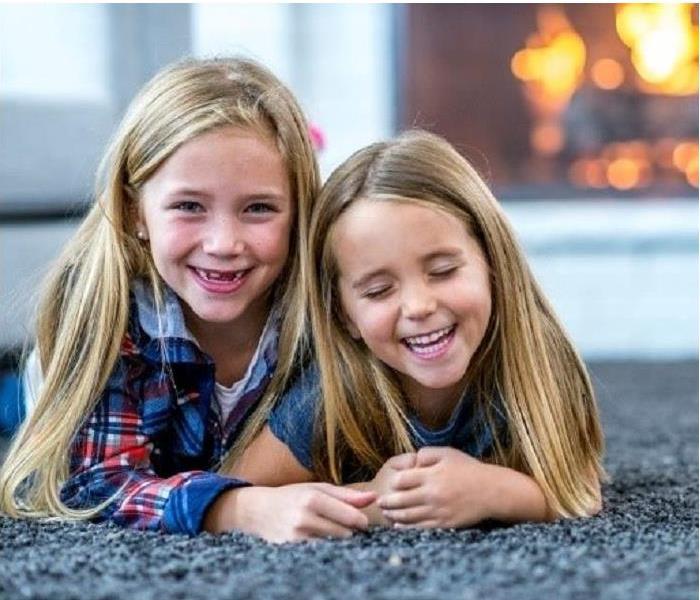 Two girls laying on carpet. Fireplace in background